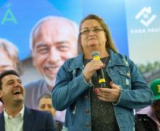 Três pessoas em um palco, com uma pessoa idosa falando ao microfone. 