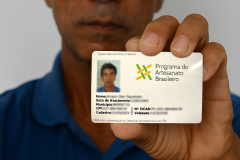 Homem segurando uma carteirinha do Programa do Artesanato Brasileiro e apontando para ela.